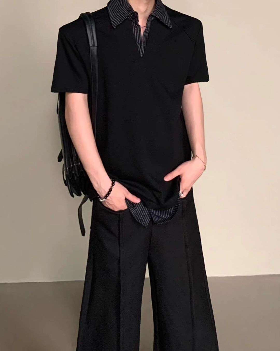 黒のモードポロトップス。半袖、ストライプ柄の折り返し衿と前立てが特徴。ワイドパンツと合わせた着用全身写真。