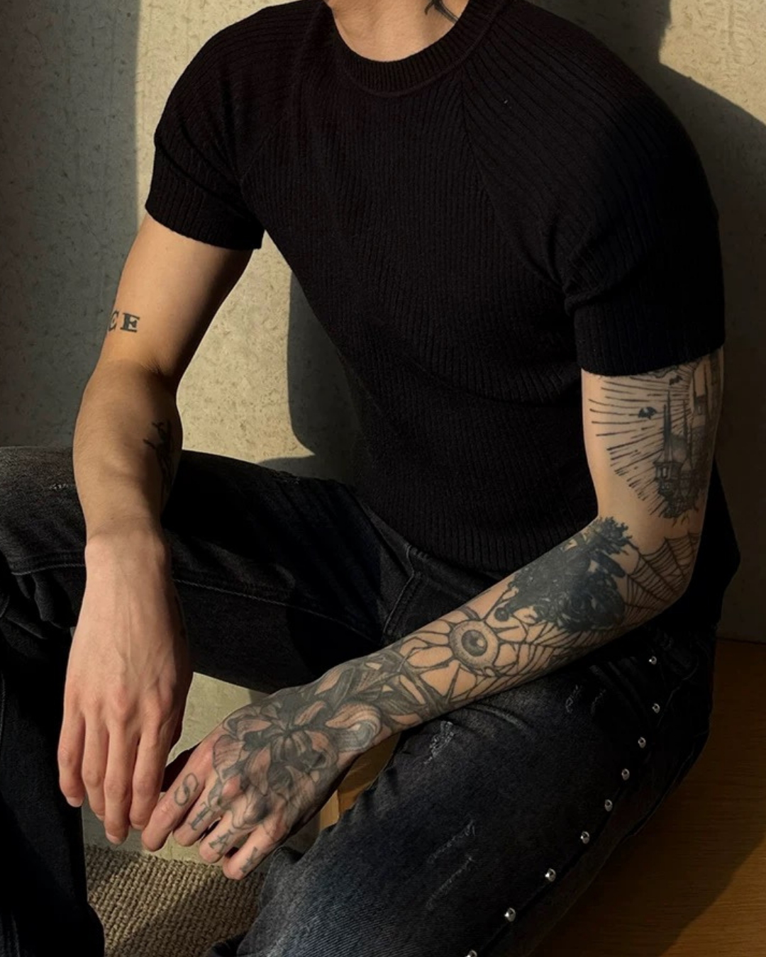 黒いリブ編みの半袖Tシャツ。クルーネック、タイトなシルエットで縦方向のリブが強調される。