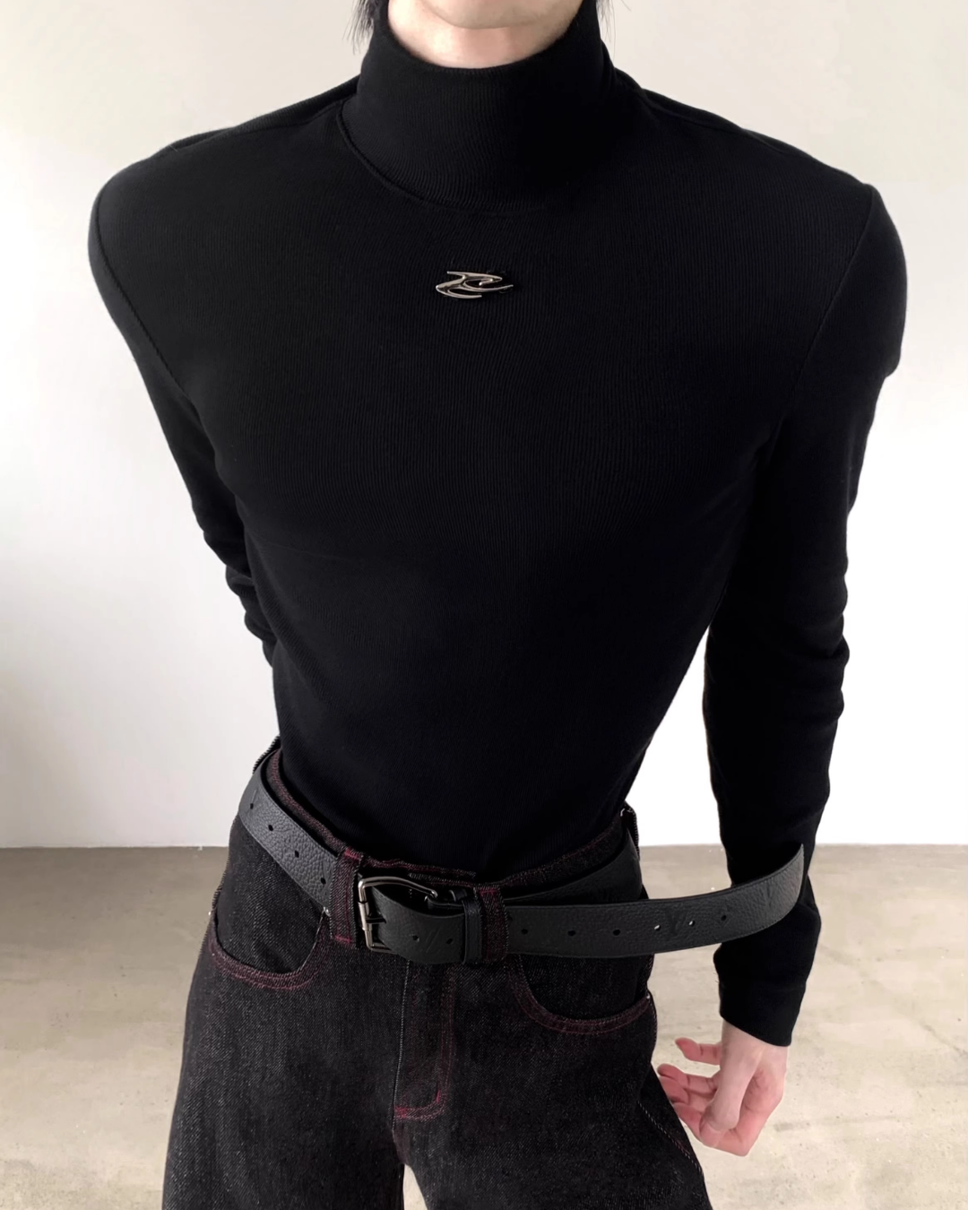 黒のリブニット素材ハイネックカットソー。胸部にシルバー色の小さなアイコン刺繍が施されている。