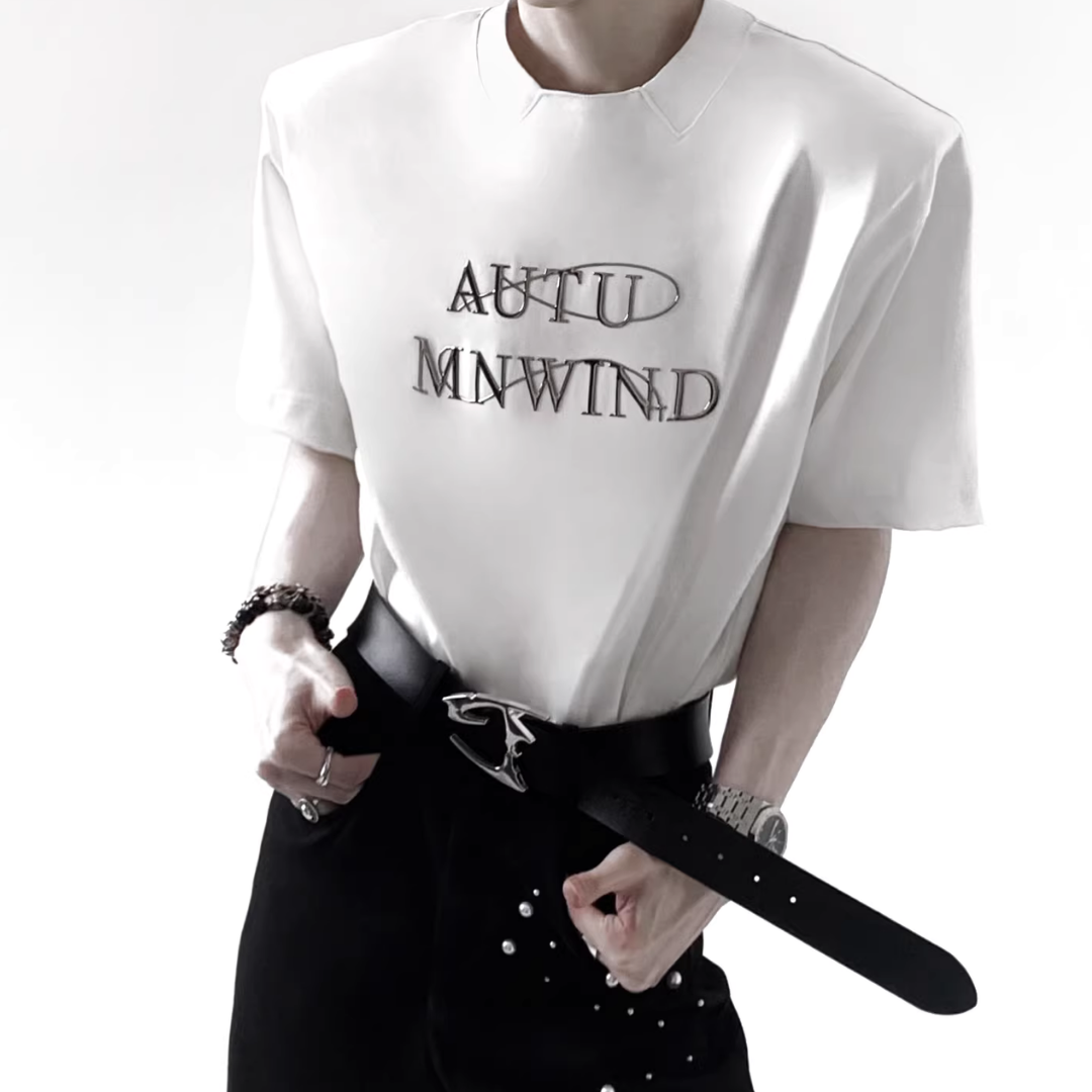 白色半袖Tシャツ。胸部にメタリックグレーのテキストロゴプリント。クルーネック、オーバーサイズシルエット。
