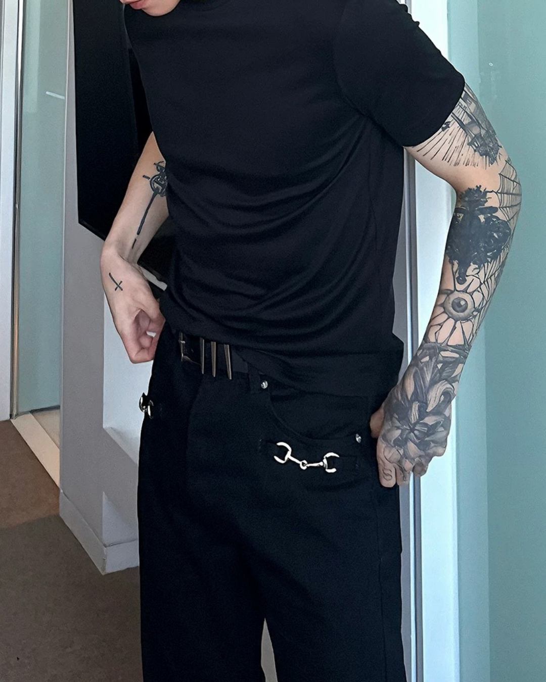 黒のオーバーサイズTシャツ。半袖で、腰部にシルバーチェーンストラップと金具装飾が施されたデザイン。