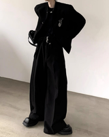 黒いテーラードジャケットとワイドパンツのセットアップ。ジャケットはオーバーサイズシルエットで刻繍装飾付き、パンツはロングで裾にタック入り。