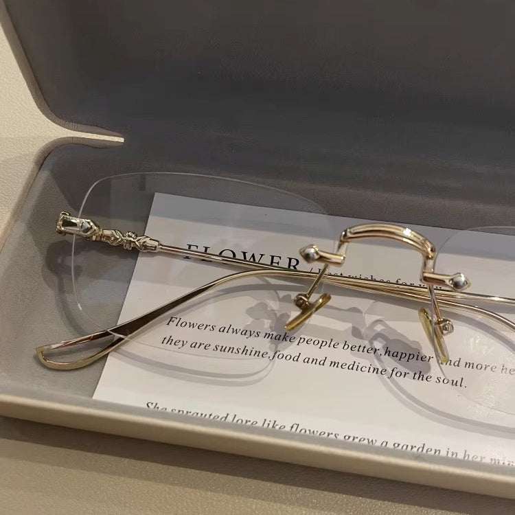 メンズのゴールドのリムレスメガネの寄り。ブリッジの金属パーツ、金色のノーズパッド、テンプル付け根の彫刻装飾、縁なしのレンズ。