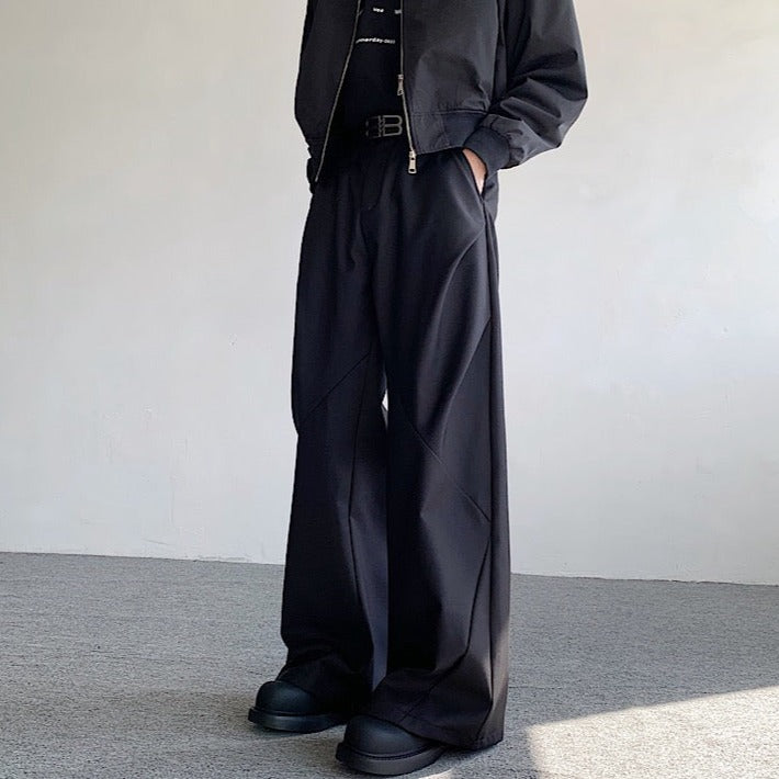 黒のワイドパンツ。ハイウエスト、ウエスト部分に細ベルト、深いポケット、床に到達する長めの着丈が特徴。