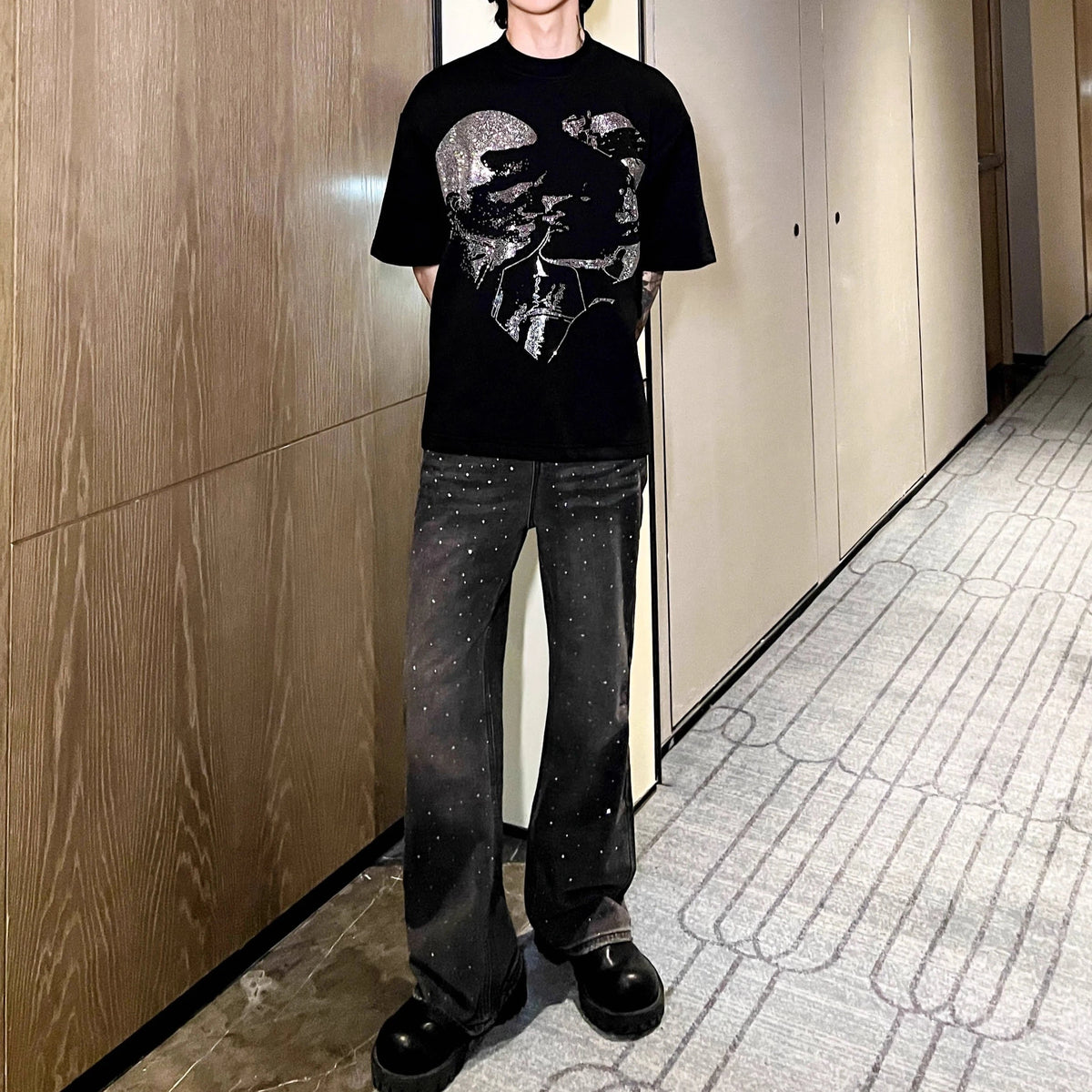 メンズの黒いクルーネックTシャツ。銀色のグラフィックプリント。黒デニムパンツにクリスタル装飾とワイドフレアシルエット。