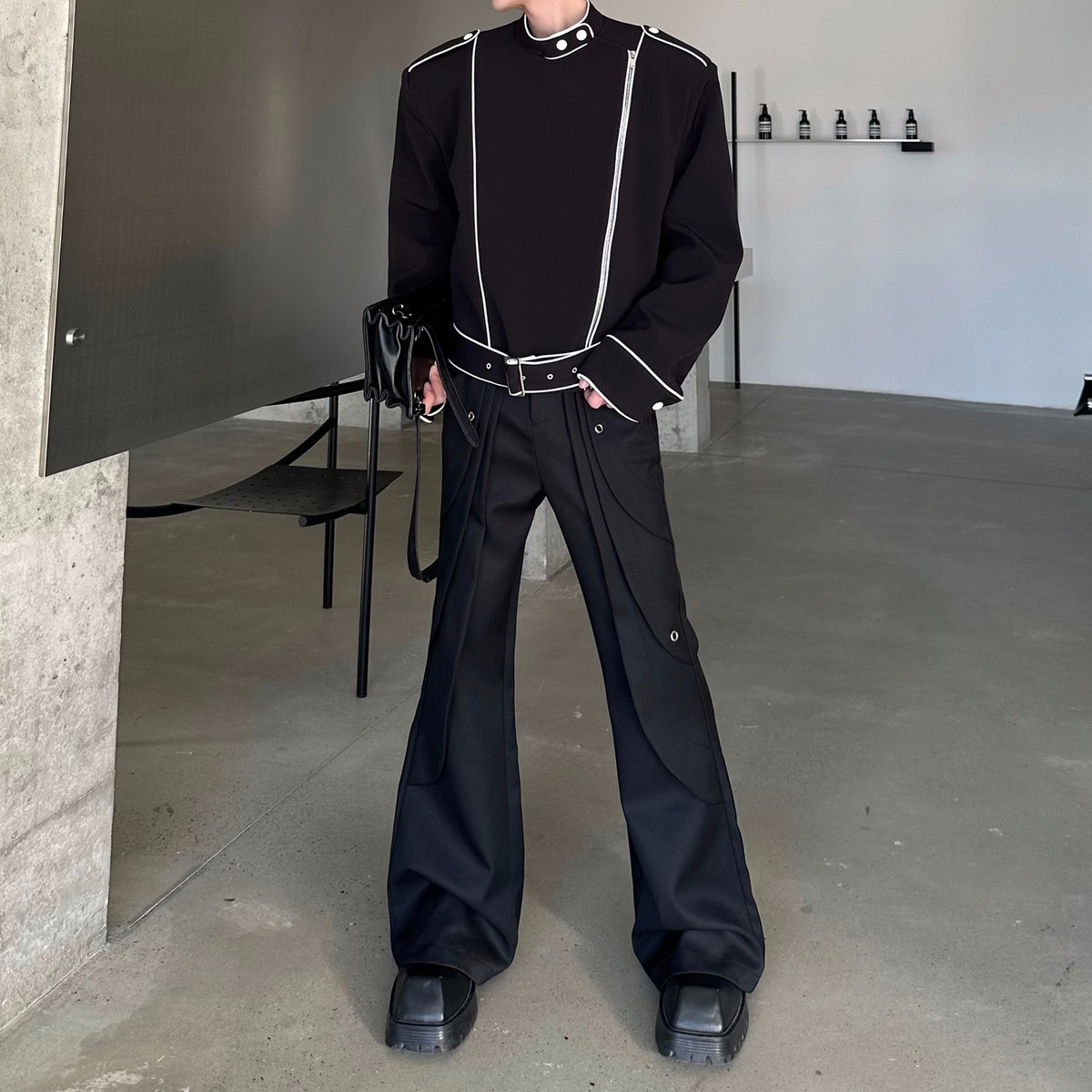 メンズの黒のフレアパンツ。腰のレイヤーとハトメ金具が見え、白パイピングの黒いショート丈トップスを合わせた全身。