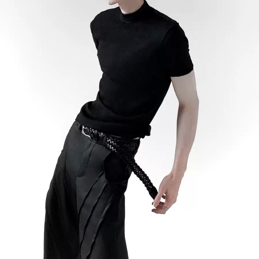 メンズの黒のハイネック半袖Tシャツ。モノトーンのプリーツスカートに編み込みベルトを合わせたコーディネート