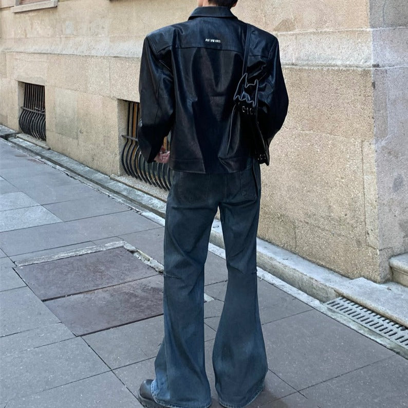メンズの黒のレザージャケット。襟付き、背中に黒いグラフィック、フロント打ち合わせ。濃紺デニムのフレアパンツと合わせた背面全身像。