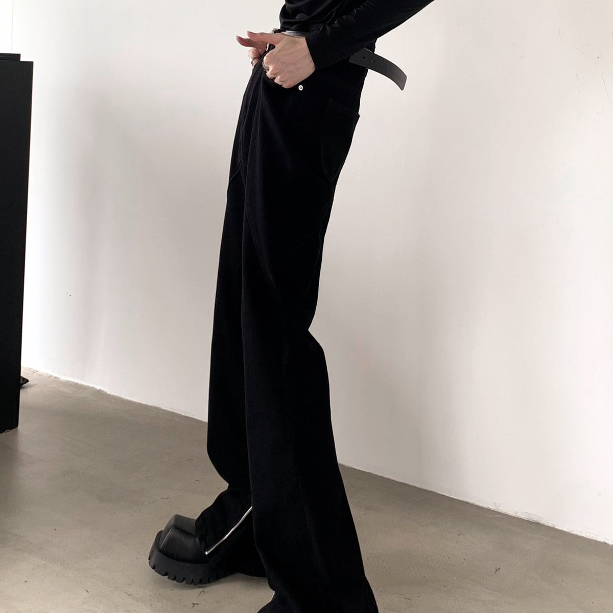 黒のワイドなパンツを横から写した着用。腰まわりにポケットがあり、すそ脇のファスナーが少し開いている。