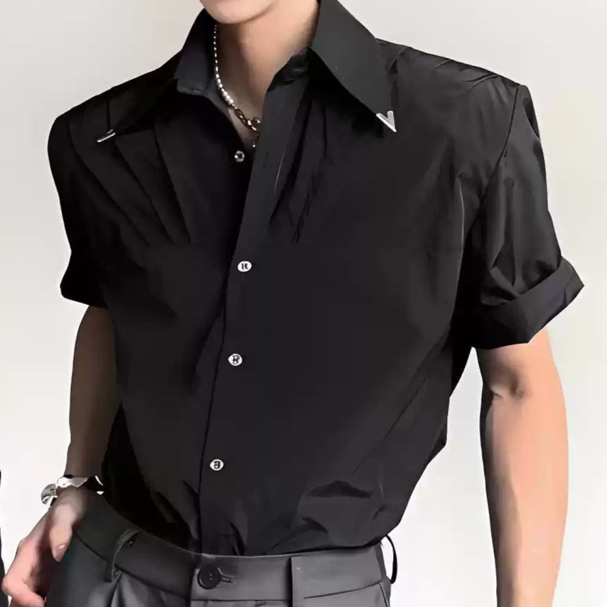 黒い半袖シャツ。広めの襟とタック入りの前立てが特徴。白い丸ボタン留めで、袖は短めにロール加工。オーバーサイズシルエット。