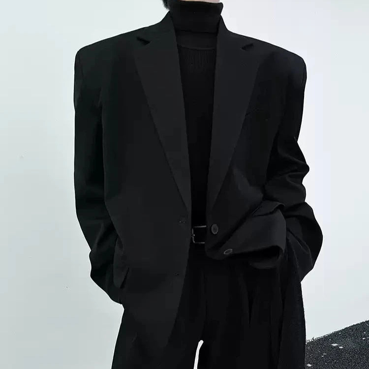 黒いオーバーサイズジャケット。ノッチ衿、長袖で肩幅に余裕を持たせたシルエット。前身頃は開いた打ち合わせ。内側に黒いタートルネックニットを重ねた着用例。