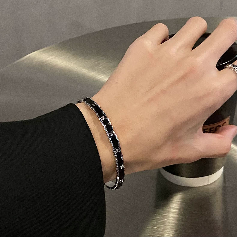 メンズの黒レザーと銀色チェーンを組み合わせたブレスレット。幅広のレザー部分にチェーン装飾が交差し、金属バックルで留める。