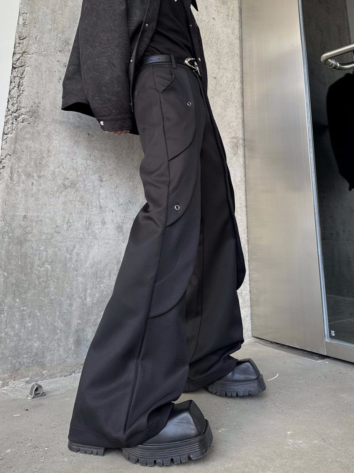 メンズの黒のフレアパンツの横向き。脇に曲線の切り替えとハトメ金具が入り、裾にかけて大きく広がる。