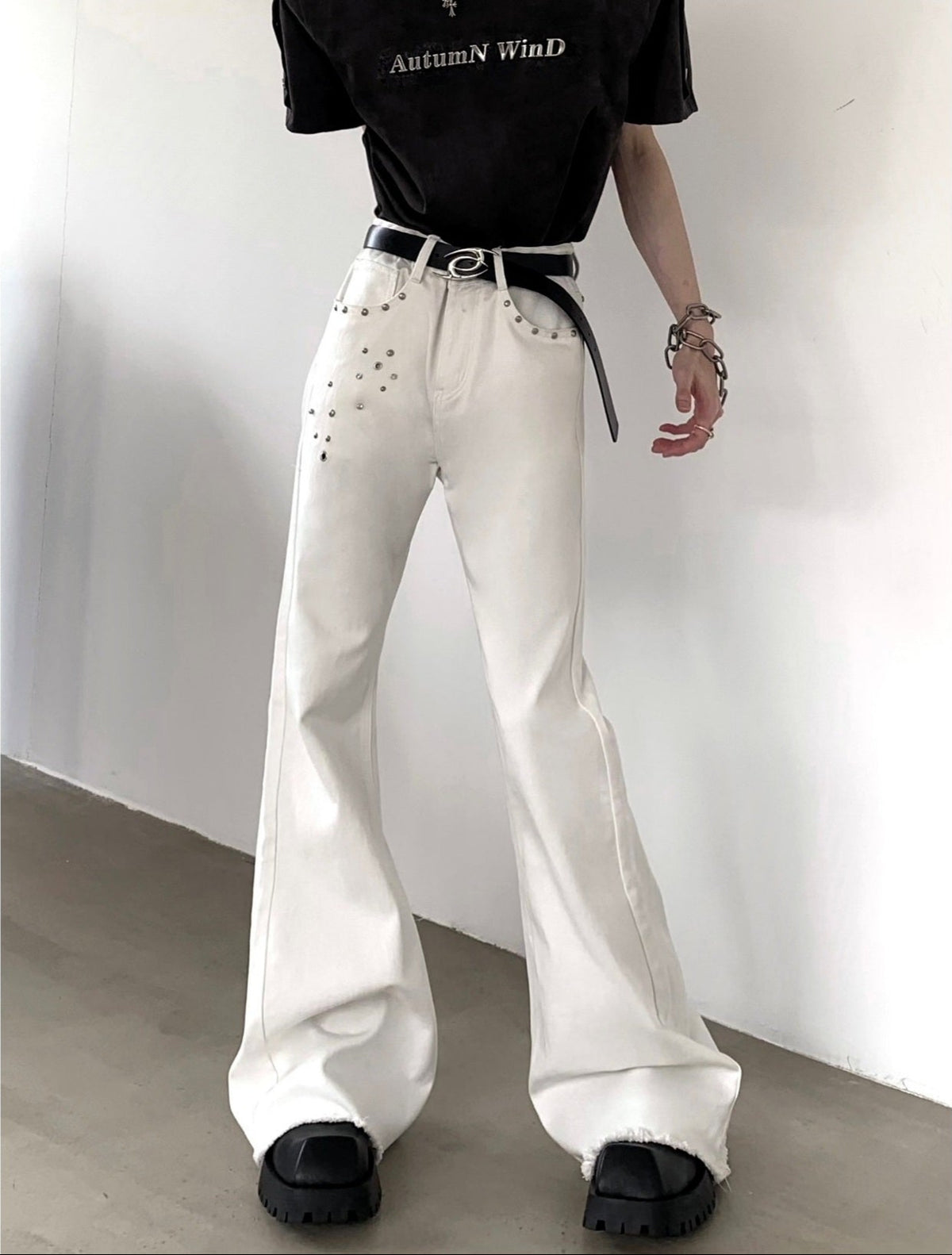 メンズの白デニムパンツ。ハイウエスト、フレアシルエット。ポケット周りにスタッズ装飾、裾はフリンジ加工。黒ベルト付き。