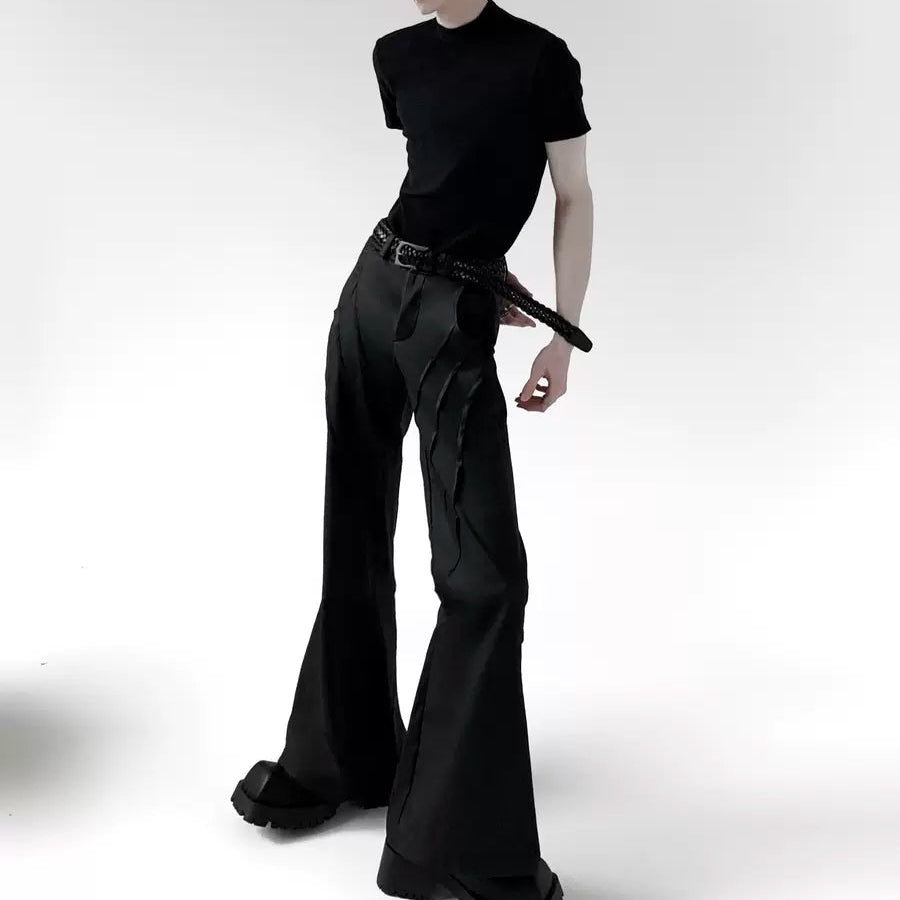 メンズの黒のTシャツと黒のフレアパンツ。パンツは裾にボリュームを持つシルエット。細身のレザーベルトを着用