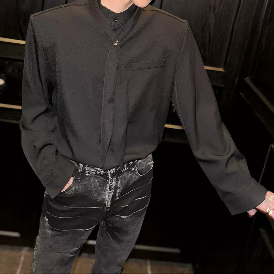 黒いスタンドカラーシャツ。長めのワイド袖と胸ポケット付き。前立てにタイデザイン装飾。