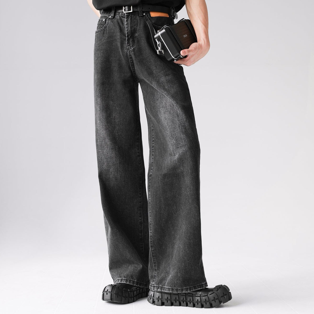 メンズの濃いグレーのワイドデニムパンツ。ハイウエストで脚部から裾にかけてドレープが入り、黒いトラクションソール付きの厚底靴との組み合わせ