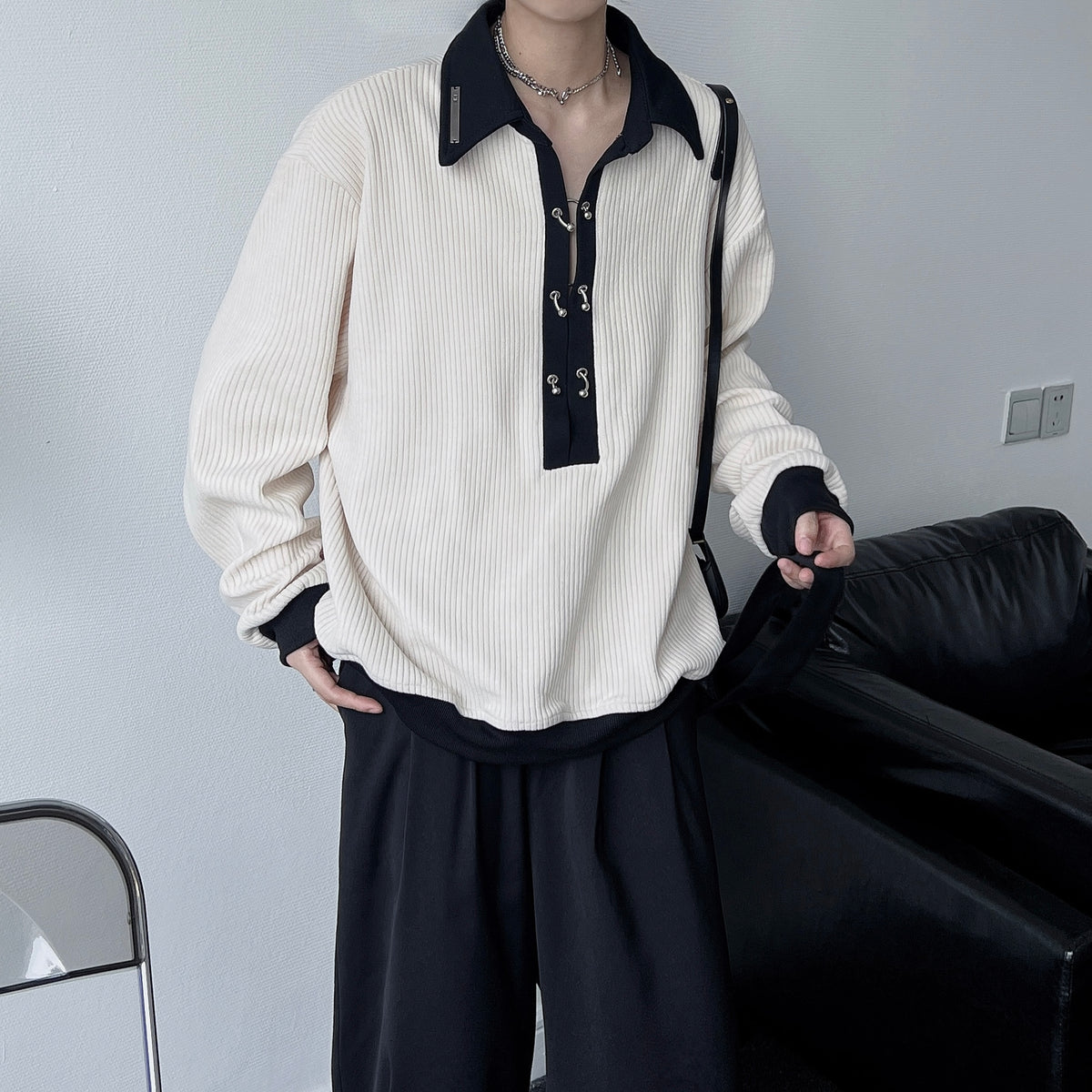 メンズの生成りのリブニット。黒い襟と黒いスカーフ風のタイ、黒い袖口をあしらったバイカラーデザイン。オーバーサイズシルエット。
