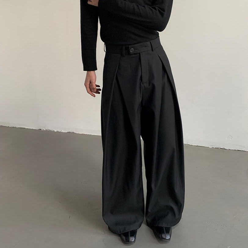黒のハイウエストスラックス。前身頃の両側にタックが入り、ウエストにベルト・ボタン付き。幅広くドレープする脚部シルエット。