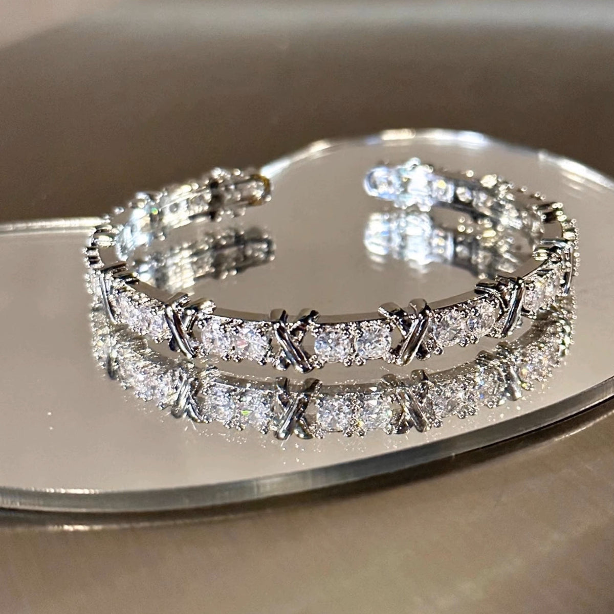 シルバートーンの金属バングル。クリアクリスタルストーンと小ぶりな幾何学模様の金属パーツを交互に配置した装飾バングル。