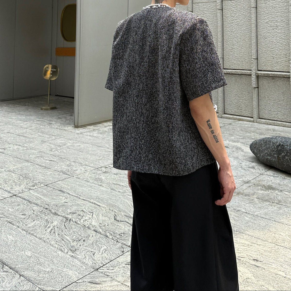 メンズの黒のツイードジャケットの後ろ姿。無地で背面に装飾はなく、肩幅のある短めの着丈に黒のワイドパンツ