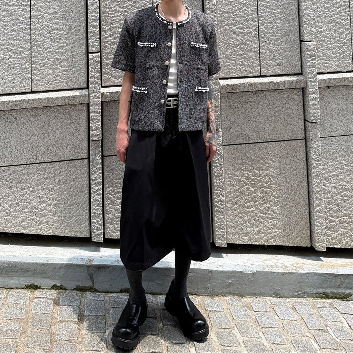 メンズの全身の正面着用。黒ツイードジャケットに、膝下丈で裾の広い黒のスカート風パンツと黒のレザーシューズ