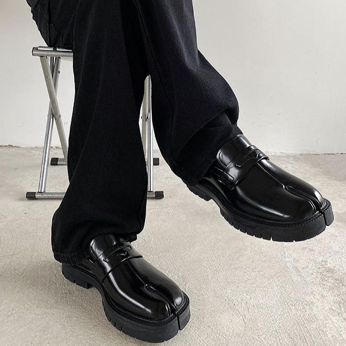 黒いエナメルレザーのローファー。厚底でリグソールが特徴。黒いワイドパンツとの重ね合わせで着用。