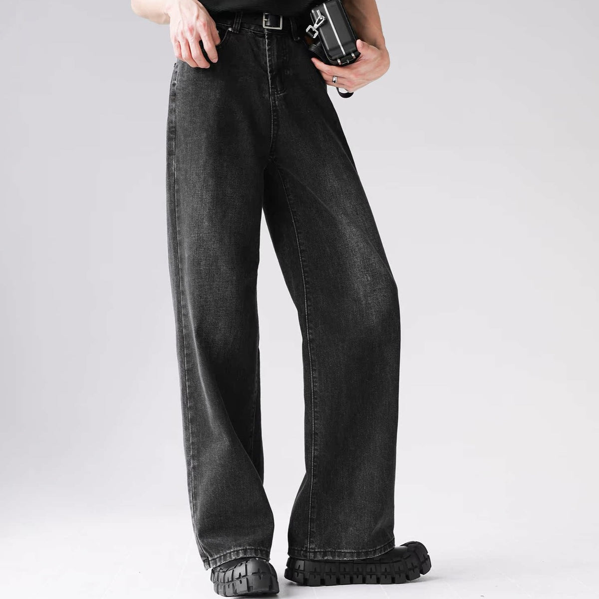 メンズの黒系デニムのワイドパンツ。ハイウエスト、ベルト付き、センターのシームラインが特徴。足首で内側に向かうドレープ感のあるシルエット。