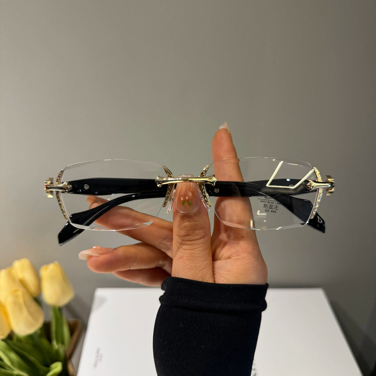 メンズの金色の金具と黒いテンプルのリムレス眼鏡を手で持った正面画像。無色透明のレンズで、ブリッジは骨形をしている。
