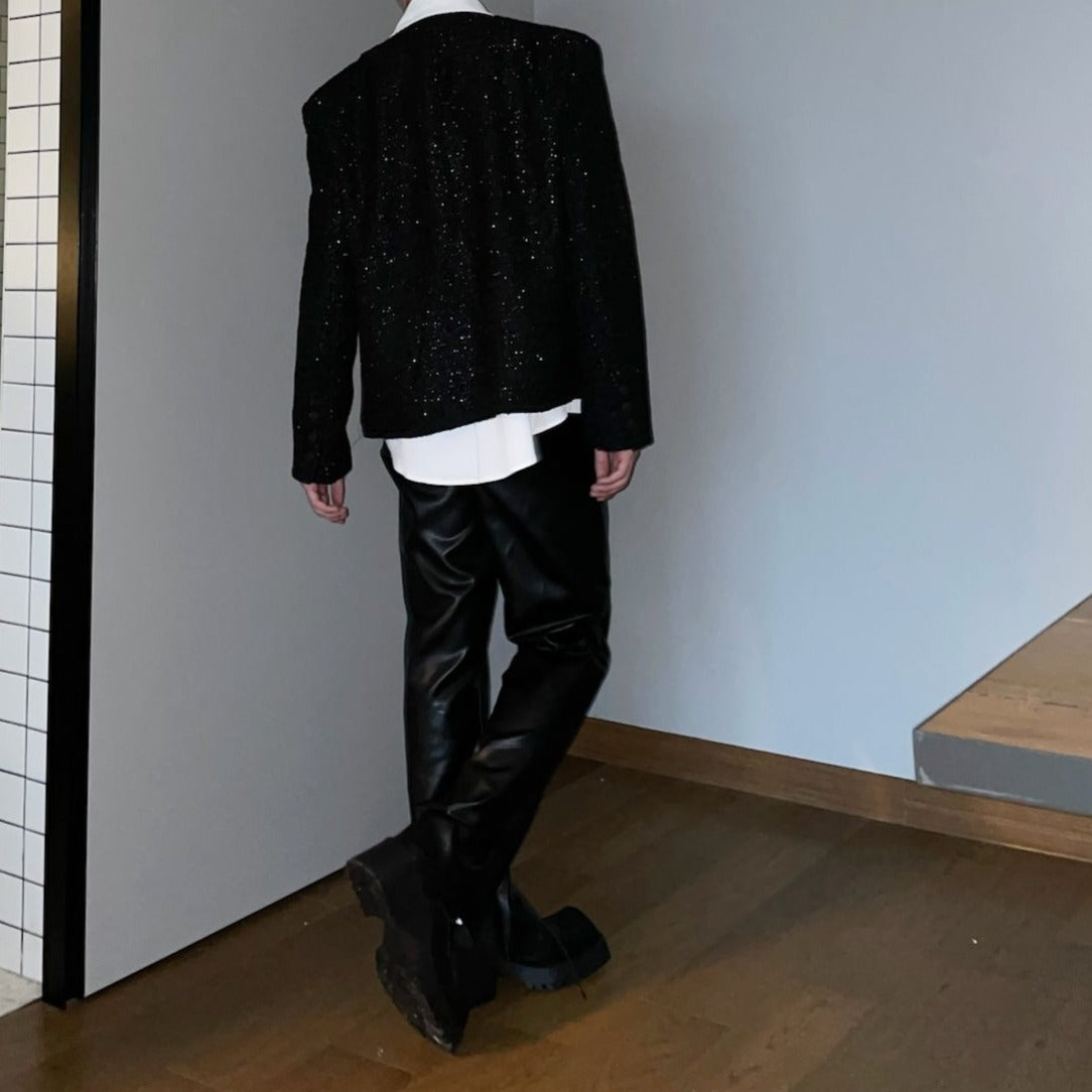 メンズの黒のラメツイードジャケット。長袖でオーバーサイズシルエット、白シャツとのレイヤード着用で、グリッターが散りばめられた素材が特徴。