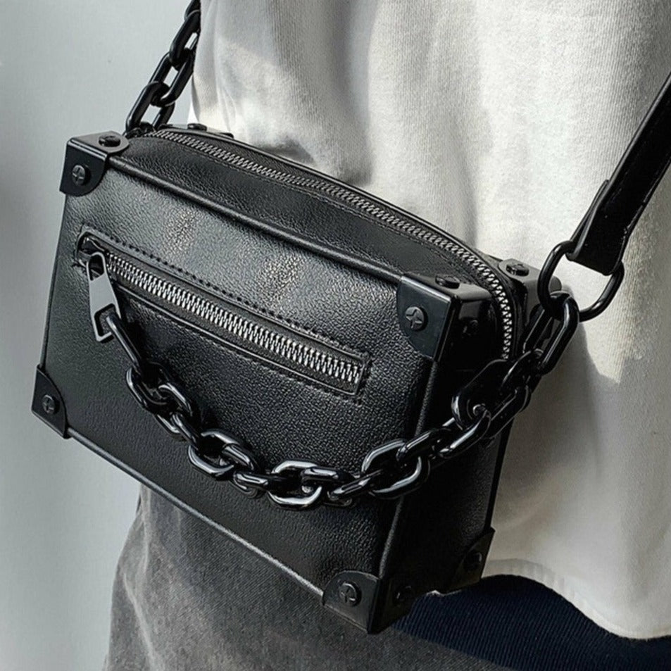 黒レザーのスクエアショルダーバッグ。金属チェーン、ジップポケット、スタッズ金具付き