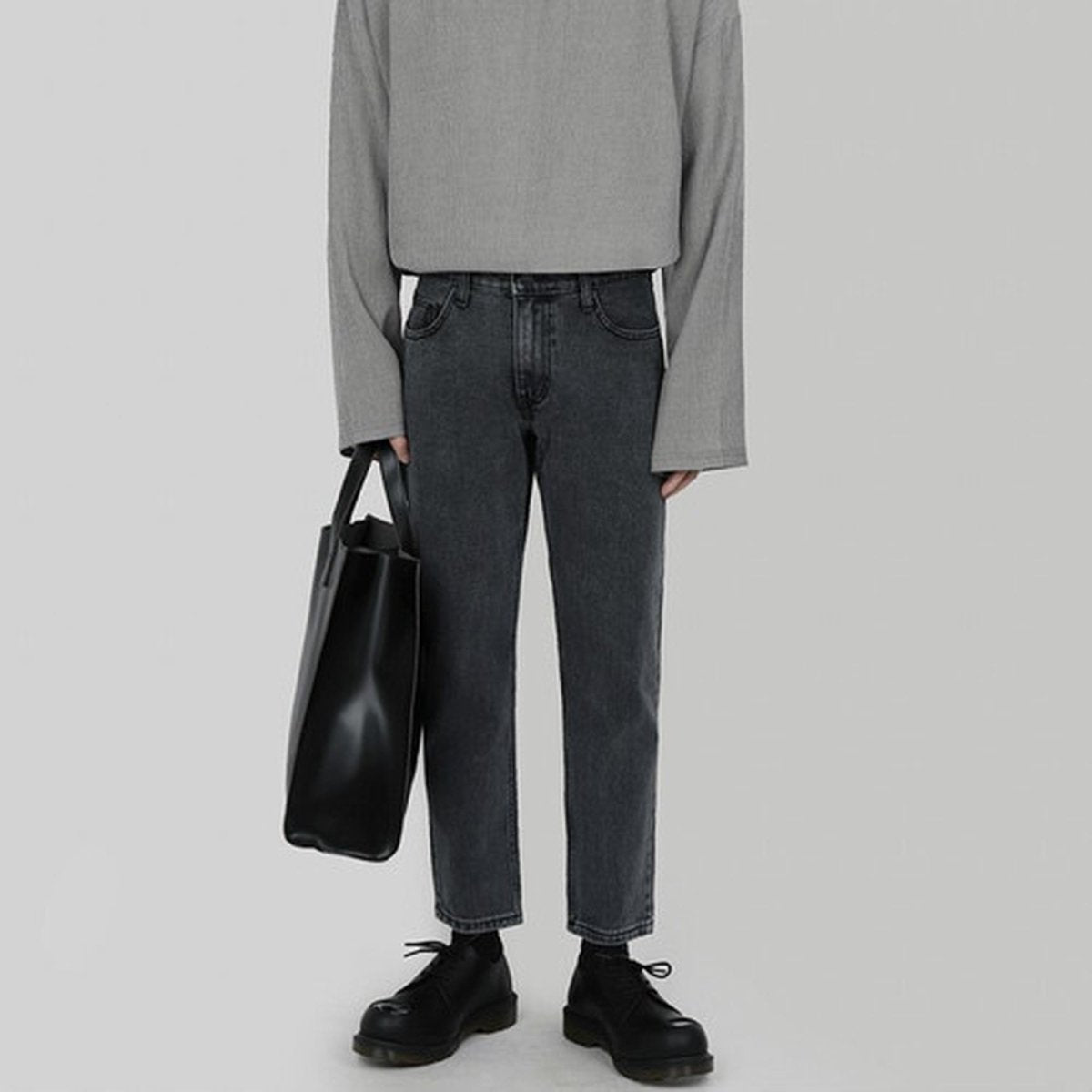 黒レザーのスクエアショルダーバッグ。ハンドル付きで、ストラップなし。デニムパンツとグレーカットソーに合わせた着用イメージ。