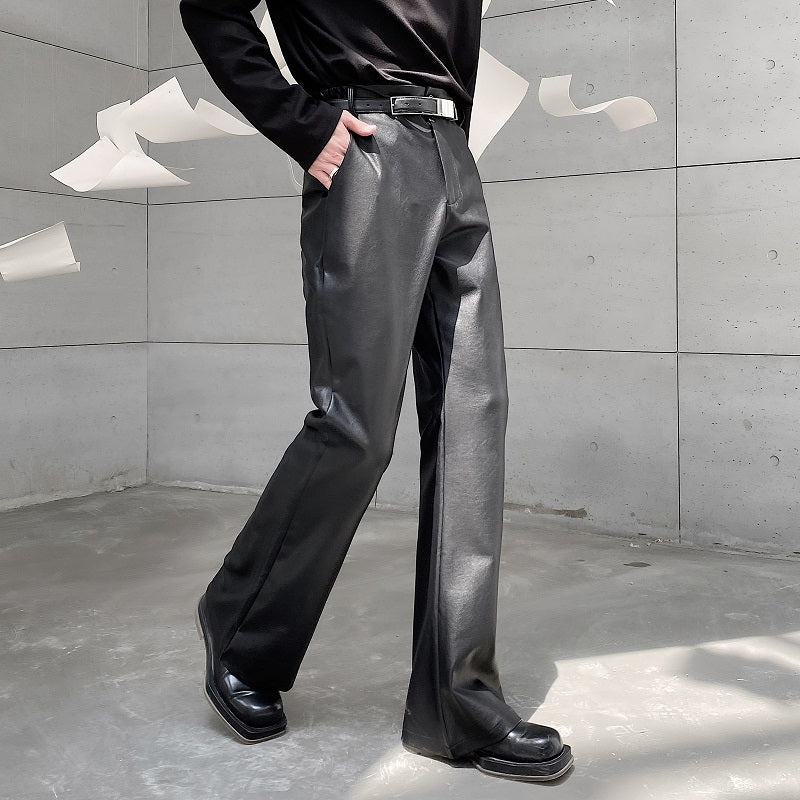 黒いレザー素材のスラックス。ハイウエストで直線的なシルエット。金属バックル付きの黒ベルト装着。光沢のある素材感。