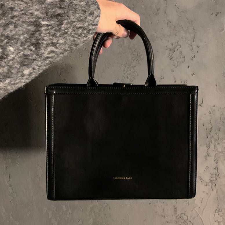 黒エナメルレザーのスクエアトートバッグ。ステッチ入りの広がったハンドルと、フロント中央に小さなロゴプレートが付く。