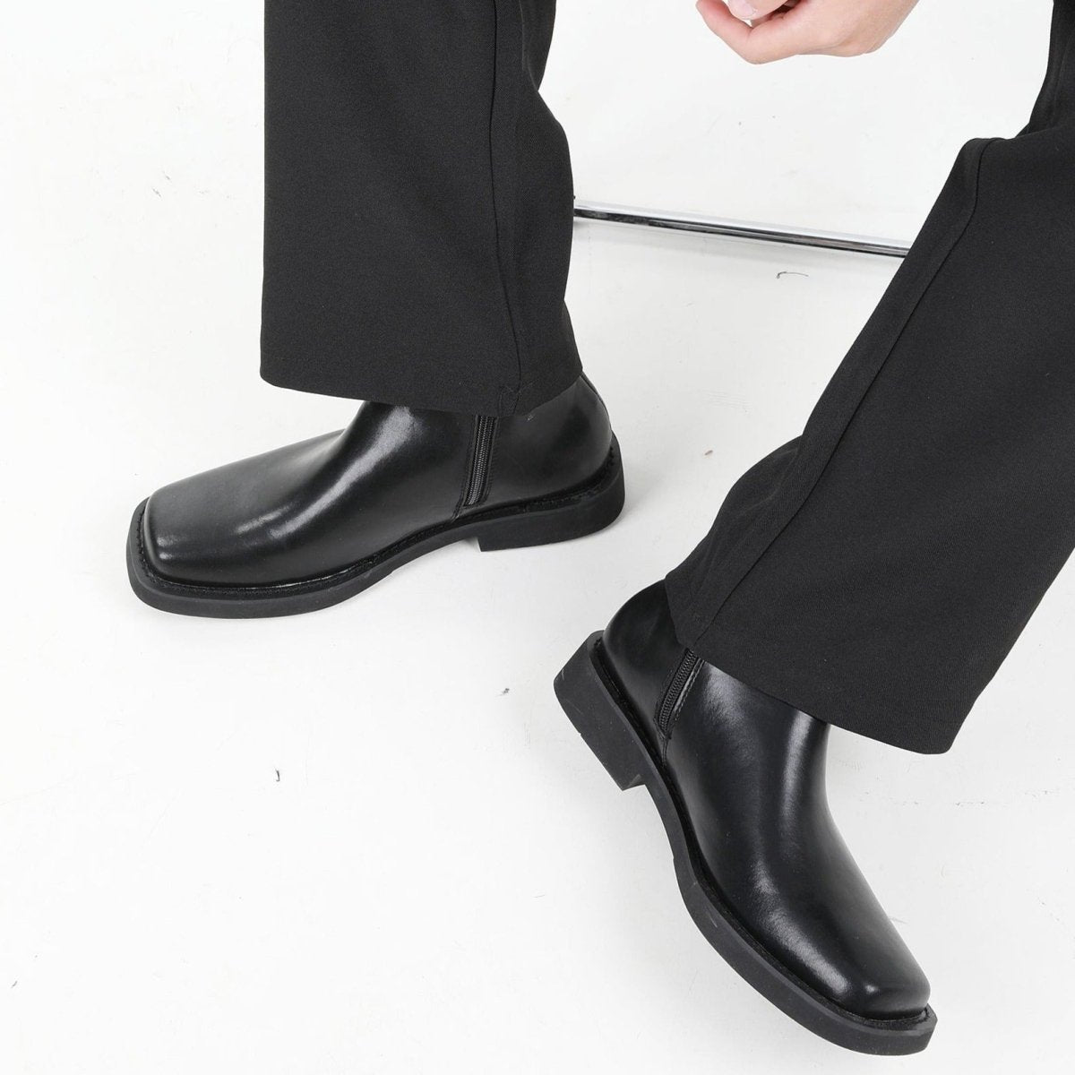 黒レザーのスクエアトゥブーツ。側面にジッパー付き、厚底ソール。黒スラックスとともにスタイリング