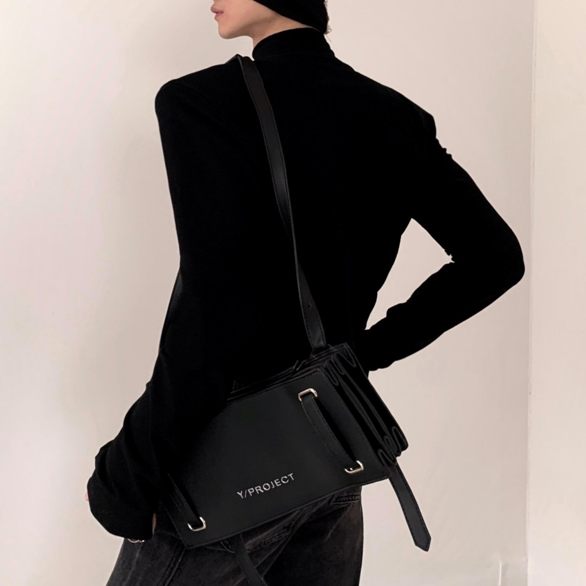 黒のハイネックカットソー。長袖でタイトなシルエット。モデルが黒レザーのショルダーバッグを肩にかけている。